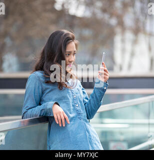 Foto von einem schönen jungen chinesischen Frau mit Handy outdoor im Straße Stockfoto