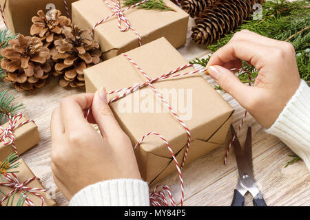Weihnachtsgeschenke Vorbereitung. Geschenkbox in Schwarz und Weiß Gestreifte Papier gewickelt, eine Kiste voller Tannenzapfen und Weihnachten Spielzeug und Verpackungsmaterial Stockfoto