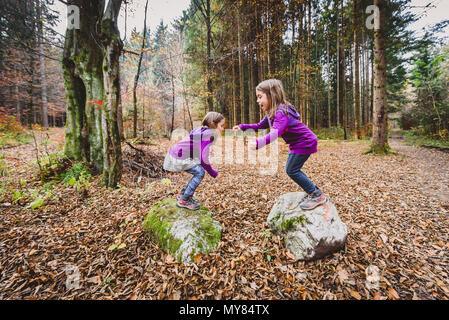 Eineiige Zwillinge sind das Springen von Felsen im Wald zu wandern. Kinder im Wald auf active Trekking in den Bergen sind Sprung von Fels zu Fels havin Stockfoto