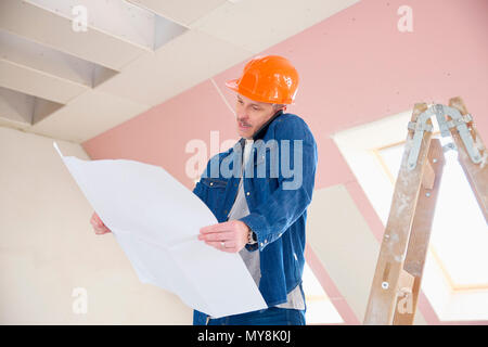 Portrait von im mittleren Alter Bauarbeiter halten sich an den Händen und sprechen auf seinem Mobiltelefon beim Stehen auf der Leiter. Stockfoto