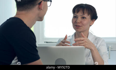 Freundliche Hündin Arzt Beratung männlicher Patient am Schreibtisch sitzt mit Laptop Stockfoto