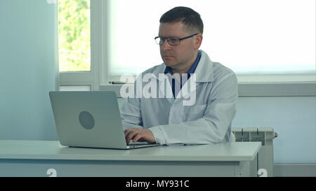 Männlicher Arzt Arbeiten am Laptop auf weißem Schreibtisch im Krankenhaus Stockfoto