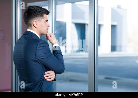 Nachdenklich, junge Geschäftsmann im Anzug durch das Fenster im Bürogebäude suchen Stockfoto