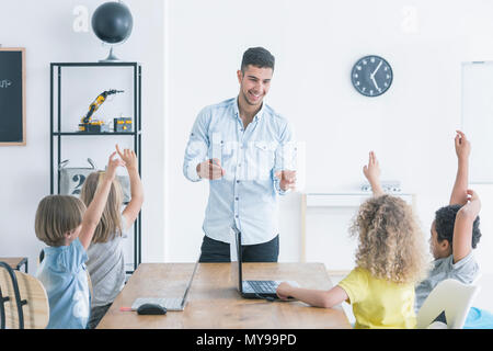 Kinder heben ihre Hände beim Informatik Unterricht bei Lehrerin zu Hause. Moderne Schule Konzept Stockfoto