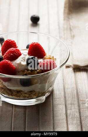 Himbeeren, Heidelbeeren, Müsli und Joghurt im Glas Schüssel auf Holzlatten. Gesundes Frühstück für ein gesundes Leben. Bild vertikal. Stockfoto