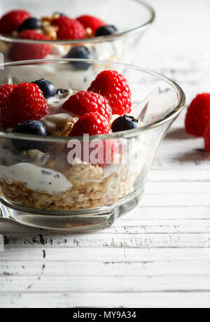 Himbeeren, Heidelbeeren, Müsli und Joghurt im Glas Schüssel auf Holzlatten. Gesundes Frühstück für ein gesundes Leben. Bild vertikal. Stockfoto
