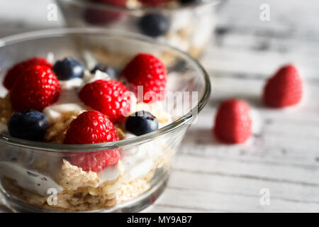 Himbeeren, Heidelbeeren, Müsli und Joghurt im Glas Schüssel auf Holzlatten. Gesundes Frühstück für ein gesundes Leben. Bild horizontal. Stockfoto