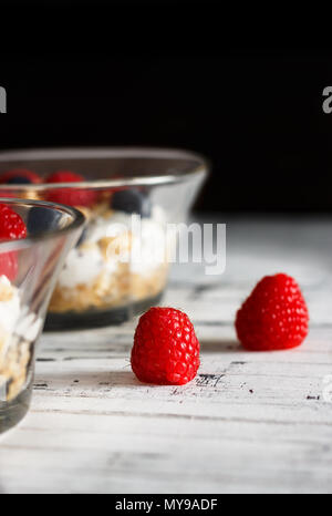 Himbeeren, Heidelbeeren, Müsli und Joghurt im Glas Schüssel auf Holzlatten. Gesundes Frühstück für ein gesundes Leben. Bild vertikal. Stockfoto