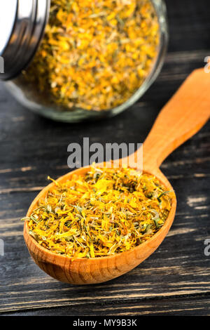 Calendula Blüten getrocknet in Gläser aus Glas und einem hölzernen Löffel auf den Tisch closeup Stockfoto