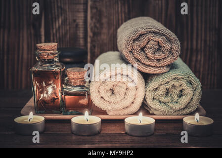 Bettwäsche mit Massage Öl in vintage Flasche, Kerzen und Stein für Stein Massage auf Holz- Hintergrund Stockfoto