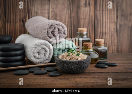 Bettwäsche mit Meersalz, Massage Öl in vintage Flasche, Kerzen und Stein für Stein Massage auf Holz- Hintergrund Stockfoto