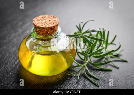 Rosemary wesentliches Öl in einer Glasflasche mit Korken Stopfen und frischem Rosmarin Kraut auf schwarzem Schiefer Hintergrund Stockfoto