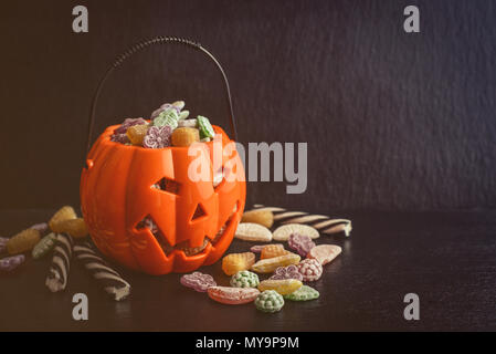 Verschiedene Süßigkeiten in Eimer in Form von Kürbis auf schwarzem Hintergrund. Halloween Konzept Stockfoto