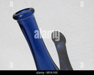 Blaue Flasche mit Schatten an weißer Wand. Stockfoto