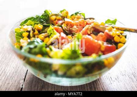 Frischer gemischter Salat in Glasschale auf hölzernen Tisch Stockfoto