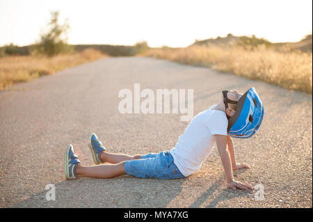 Schönes kleines Kind tragen Sport Helm sitzen auf leere Straße Stockfoto