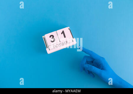 Farbige Hand zeigen auf hölzernen Kalender 31 Oktober Datum. Halloween blau minimal Kreativurlaub Konzept. Stockfoto