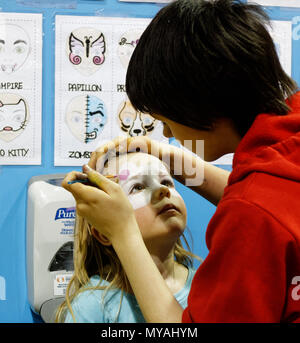 Eine Frau Kinderschminken ein kleines Mädchen (3 Jahre alt) als Hello Kitty bei einem Kinderfest Stockfoto