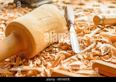 Meißel in Holzspäne auf den Schreibtisch gelegt. Carving Tools in der Späne liegen. In einem Carving Workshop. Schneiden von lindenholz. Holz- Hammer auf einer wor Stockfoto