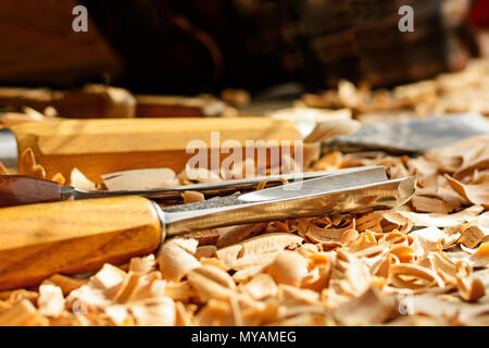 Meißel in Holzspäne auf den Schreibtisch gelegt. Carving Tools in der Späne liegen. In einem Carving Workshop. Schneiden von lindenholz. Stockfoto