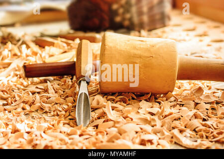 Meißel in Holzspäne auf den Schreibtisch gelegt. Carving Tools in der Späne liegen. In einem Carving Workshop. Schneiden von lindenholz. Holz- Hammer auf einer wor Stockfoto