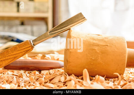 Meißel in Holzspäne auf den Schreibtisch gelegt. Carving Tools in der Späne liegen. In einem Carving Workshop. Schneiden von lindenholz. Holz- Hammer auf einer wor Stockfoto