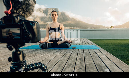 Blogger Aufnahme Inhalt zu Yoga und Meditation für Ihren Blog auf Kamera auf der Terrasse Ihres Hauses sitzend mit malerischem Hintergrund. Kamera montiert Stockfoto