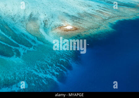 Blick aus der Vogelperspektive auf das große, farbenfrohe Korallenriff, das die winzige weiße Sandbank-Insel mit zwei Booten in der Nähe umgibt Stockfoto
