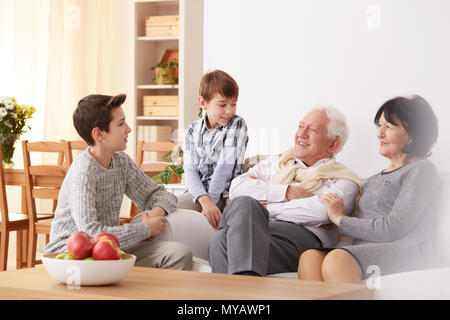 Lächelnden jungen sprechen mit ihren Großeltern in einem Wohnzimmer Stockfoto