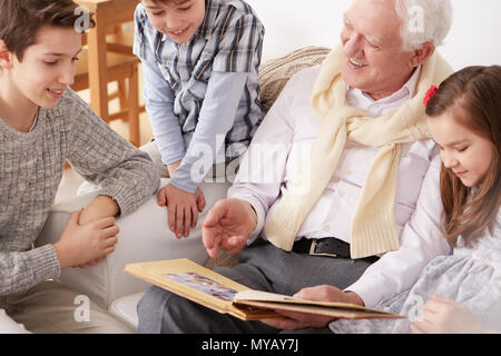 Glückliche Kinder sitzen auf einem Sofa mit Großvater Holding ein Fotoalbum Stockfoto