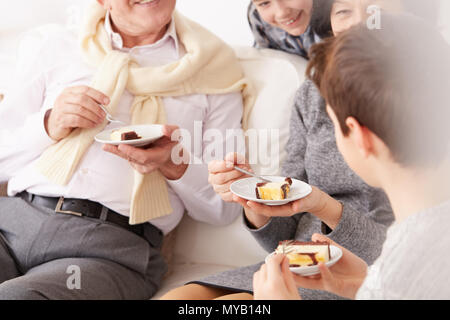 Großeltern und Enkel sitzt auf einem Sofa und essen einen Kuchen Stockfoto
