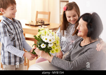 Gerne Enkelkinder geben einen Blumenstrauß für Ihre Oma sitzend auf einem Sofa Stockfoto