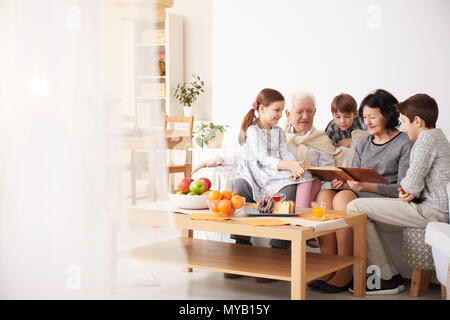 Glückliche Großeltern, Fotoalbum, um ihre Enkelkinder in einem Wohnzimmer Stockfoto