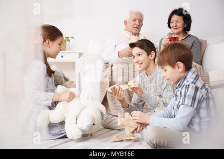 Kinder spielen auf einer Etage und ihre Großeltern sitzen auf einem Sofa Stockfoto
