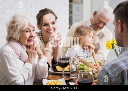 Glückliche Familie sitzt am Tisch beim Abendessen, Enkelin sitzen auf's Großvater schoß Stockfoto