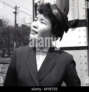 1950, historische, Nahaufnahme einer japanischen Frau Reiseführer tragen Uniform und Mütze stehend außerhalb ihrer touristischen Reisebus in Tokyo City Center, Japan. Diese Leitfäden wurden weibliche Personen, die mit Touristen auf dem Bus gereist und wies auf verschiedene Teile der Stadt und es gab den Besuchern aus Übersee im Allgemeinen zu helfen. Stockfoto