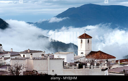 Die alpujarran Dorf Capileira, mit der Katholischen Kirche ist eingehüllt in Nebel, hoch oben in den Bergen der Sierra Nevada in der spanischen Region Andalusien. Stockfoto
