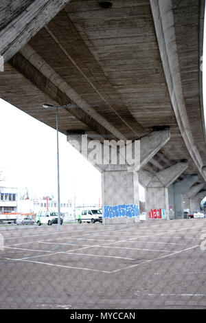 Ein eingezäunter Parkplatz in der Stadt unter einer Brücke mit Lanes eine Hauptstraße. Stockfoto