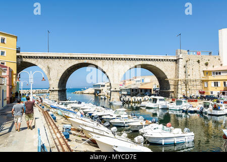Der kleine Fischerhafen von Endoume von einem sonnigen Morgen mit seinen Booten und Restaurants und die Straße Brücke der Kennedy Corniche. Stockfoto