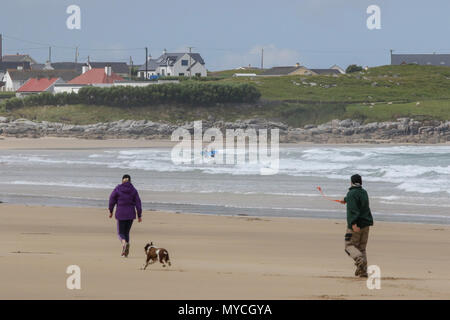 Mann Frau und Hund auf der Jagd nach einem Ball am Strand in Irland. Der Strand mit zwei bodyboardern ist bei Ballyhiernan, County Donegal, Stockfoto