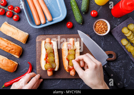 Foto oben von zwei Würstchen auf Schneidebrett auf Tabelle mit menschlichen Händen Stockfoto