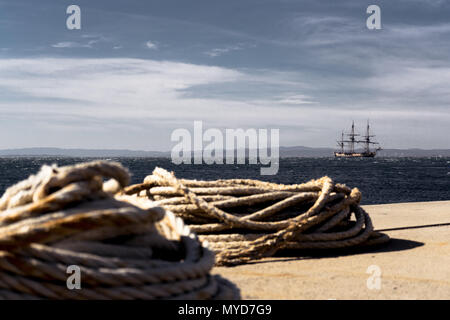 Alte hölzerne Segelboot mit drei Masten offshore verankert, warten auf den Sturm zu beruhigen. In der Vorderen liegen ein paar lange Seile auf den Boden. Stockfoto