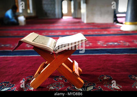 Koran auf Stand auf dem roten Teppich und verschwommenes Innenraum einer Moschee im Hintergrund Stockfoto