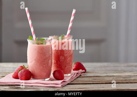 Joghurt und Erdbeere Smoothie in zwei Gläser mit Trinkhalm auf hölzernen Tisch Stockfoto