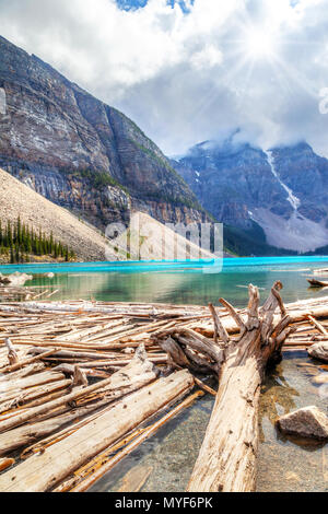 Treibholz am Ufer des Lake Moraine mit Sun spähen durch die Wolken überschatten die Berge von Tal der zehn Gipfel. Stockfoto