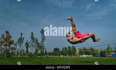 Austrickst, auf Rasen im Park. Der Mensch macht Salto vor. Kampfkunst und Parkour. Street Workout. Stockfoto