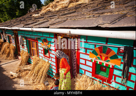 Indische Frau und seine typischen kumaoni Haus, wo ein Haufen Weizen trocknen in der Sonne ist, Kala Agar Dorf, Kumaon Hügel, Uttarakhand, Indien Stockfoto