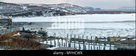 Panoramablick auf die alte Werft, Produktion Rümpfe, alte Boote, Schiffe, Bucht mit Eis, schneebedeckte Hügel bedeckt, die Felsen in der Ferne im April nach Stockfoto