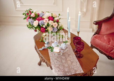 Dekoriert vintage Tabelle in weißen barocken Interieur mit roten Luxus Sofa. Tabelle ist für romantische Ereignis eingestellt. Stockfoto