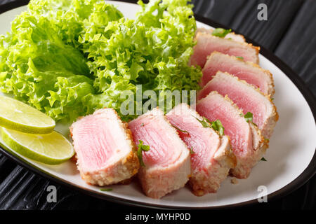 Ahi Thunfisch paniert serviert mit Salat und Kalk in der Nähe auf einer Platte auf einem Schwarzen Tisch. Horizontale Stockfoto